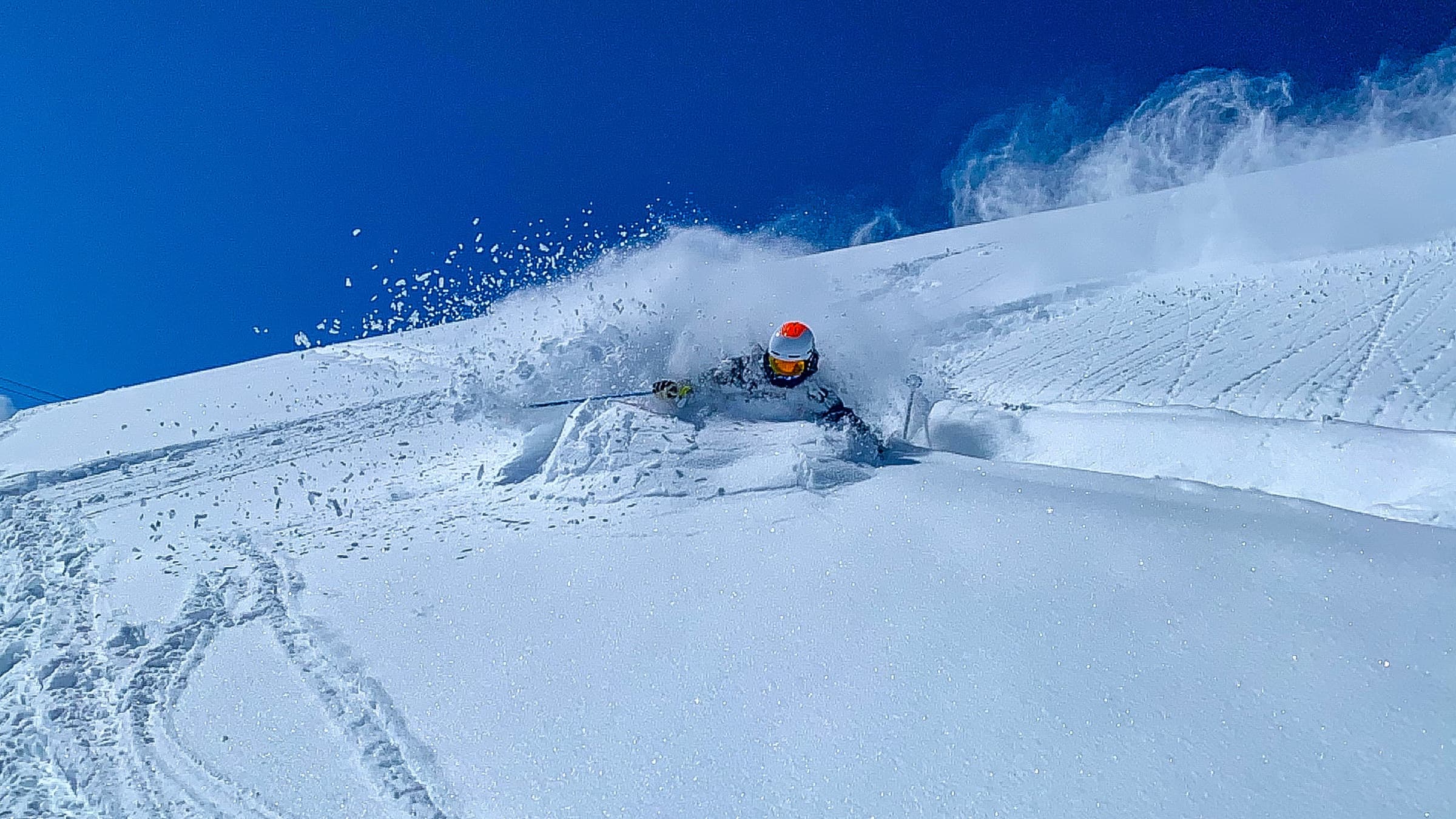 William skiing in deep powder under a clear blue sky